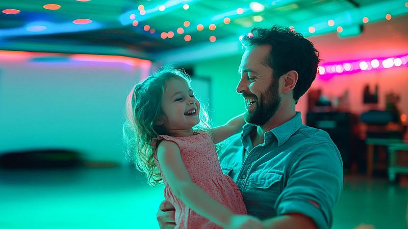 Mann mit Tochter auf dem Arm und tanzt im Discolicht