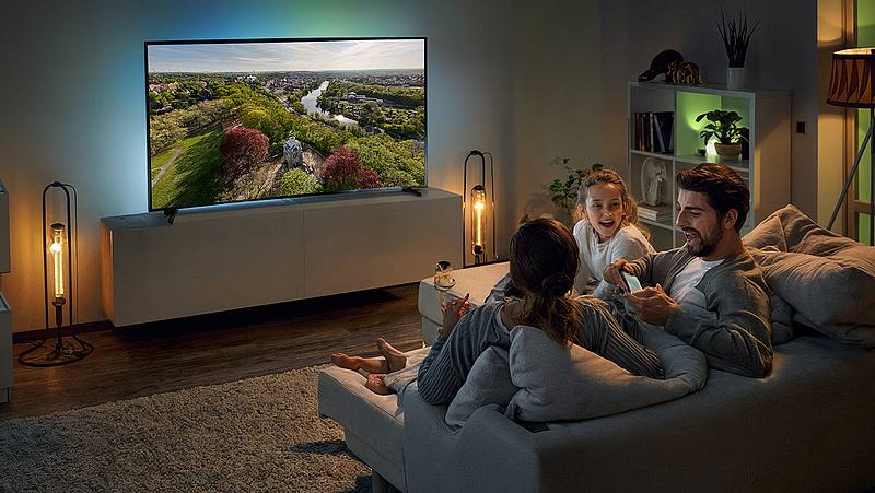 Dunkles Wohnzimmer mit gemütlicher Beleuchtung und einer Familie beim Fernsehabend
