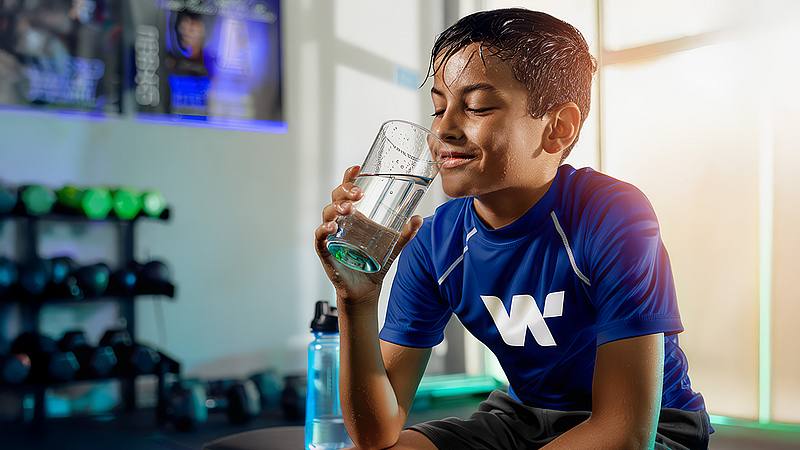 ein Junge im blauen Fußballtrikot ist verschwitzt und trinkt ein Glas Wasser